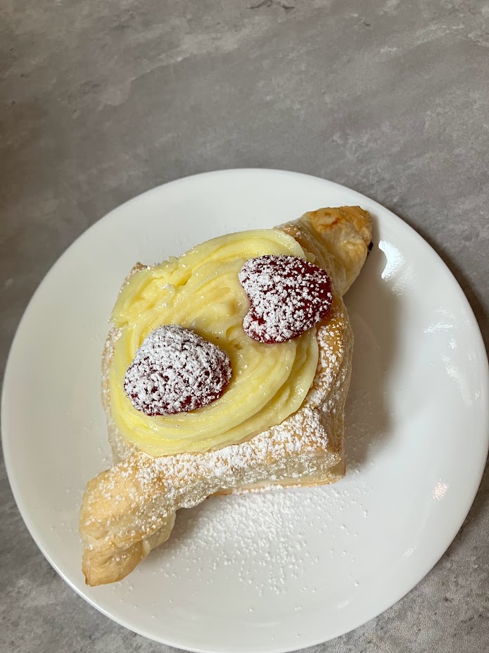 lemon creme pattisserie tart. Pastry filled with lemon cream and topped with red raspberries coated in powdered sugar. Pastry on a white plate with grey background.